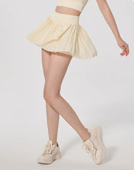 Person wearing a light yellow pleated skirt and matching sneakers on a plain background