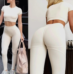 Woman wearing a white athletic outfit with leggings and a crop top, holding a pink bag.