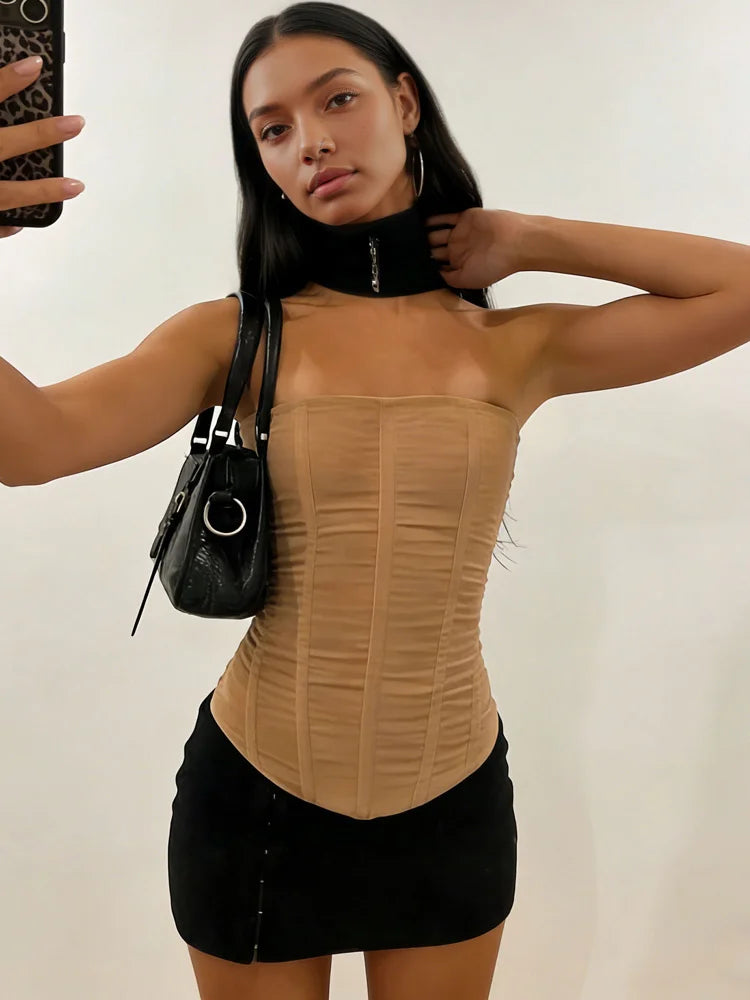 Woman wearing a khaki top and black skirt with a black handbag against a plain background