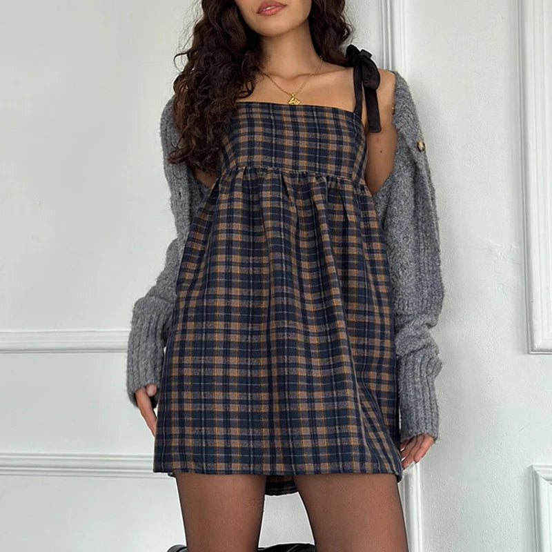 Woman wearing a plaid dress and gray cardigan against a white wall