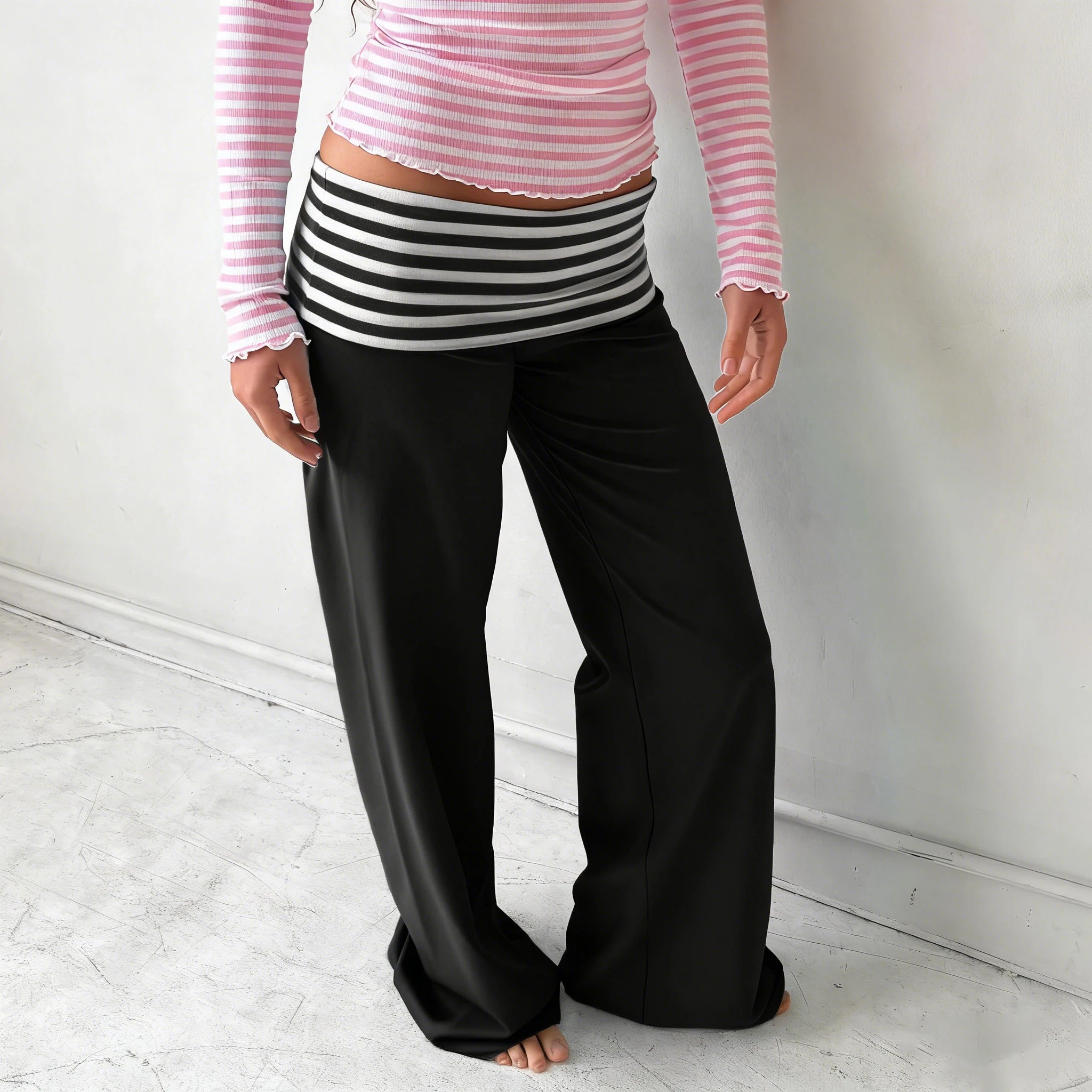 Person wearing a pink and white striped shirt with black and white striped shorts and black wide-leg pants on a light wooden floor.