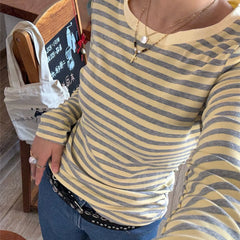 Person wearing a yellow and gray striped shirt with a necklace, sitting in a casual setting.