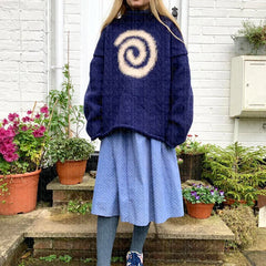 Person wearing a blue sweater with a spiral design in front of potted plants.