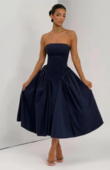 A woman modeling a strapless navy blue midi dress with a structured corset-style bodice and a full, gathered skirt, standing against a plain light gray studio background.