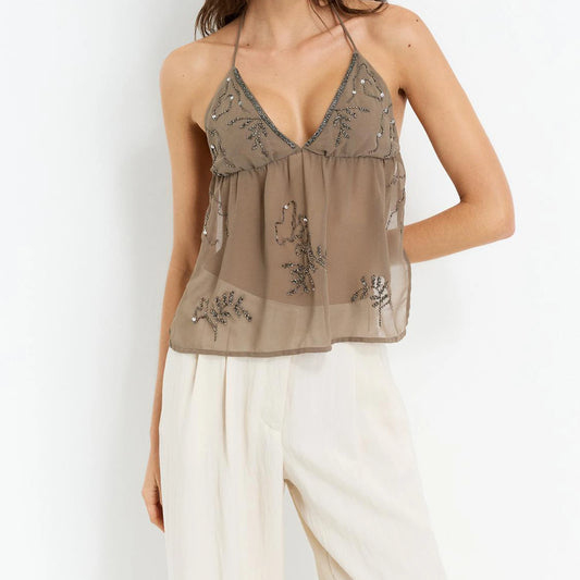 Woman wearing a beige embroidered top and white pants on a plain background