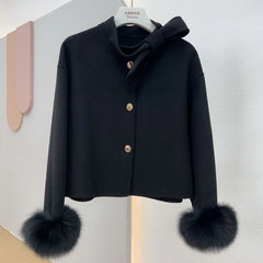 Black coat with fur cuffs on a hanger against a light gray background