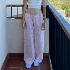 Person wearing a white top and light pink pants on a balcony.