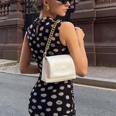 Woman in a polka dot dress holding a white handbag with a gold chain strap.