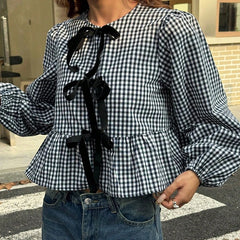 Person wearing a black and white checkered blouse with ruffled sleeves and black ribbons, standing outdoors.