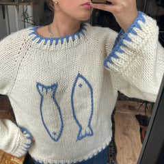 Person wearing a white sweater with blue fish designs, taking a mirror selfie.