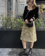 Person wearing a black jacket and yellow patterned skirt standing outdoors.