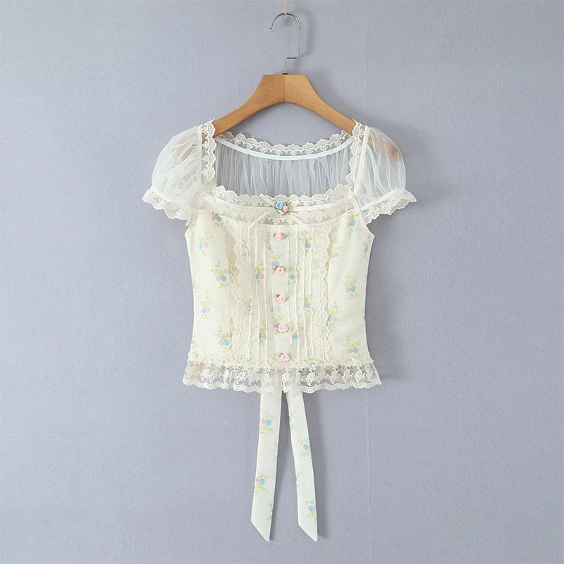 White lace top with floral details on a wooden hanger against a gray background