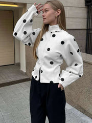 Woman wearing a white jacket with black polka dots and black pants outdoors.