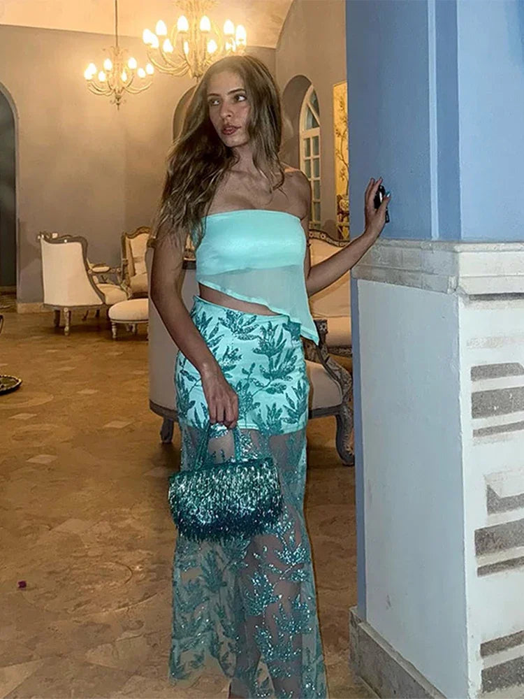 Woman in a light blue strapless top and green patterned skirt standing in an elegant room.