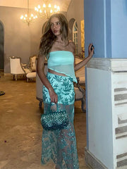 Woman in a light blue strapless top and green patterned skirt standing in an elegant room.