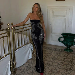 A woman wearing a sparkling black maxi dress with a strapless design and a flowing silhouette, perfect for a special occasion.