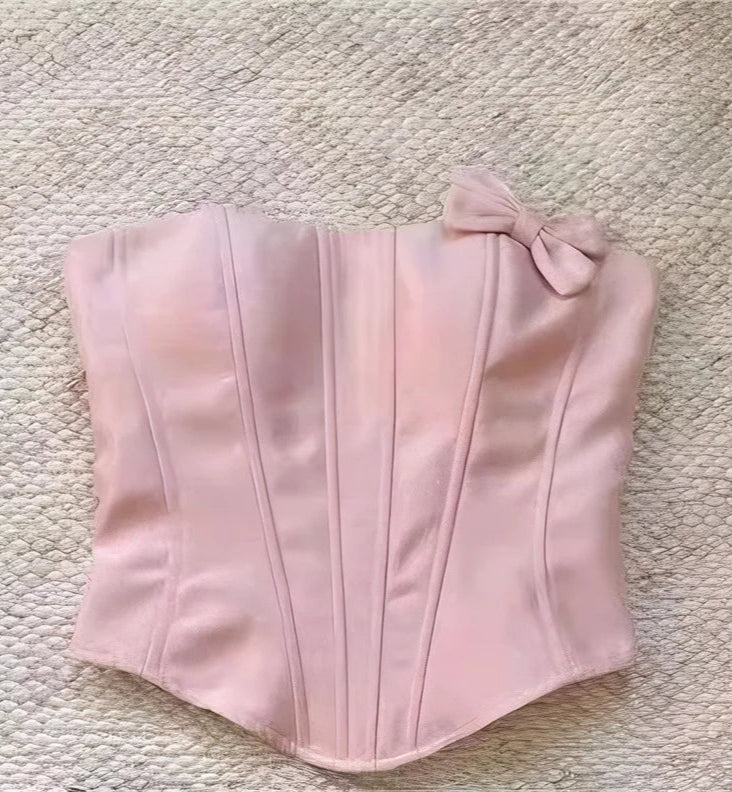 Pink corset with a bow on a textured beige surface
