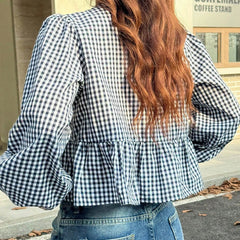 Person wearing a black and white checkered blouse with ruffled details, standing outdoors.