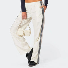 Person wearing white pants with black stripes and holding a beige handbag 