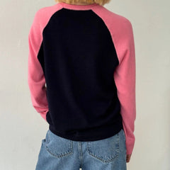 Person wearing a pink and black baseball-style sweatshirt with blue jeans 