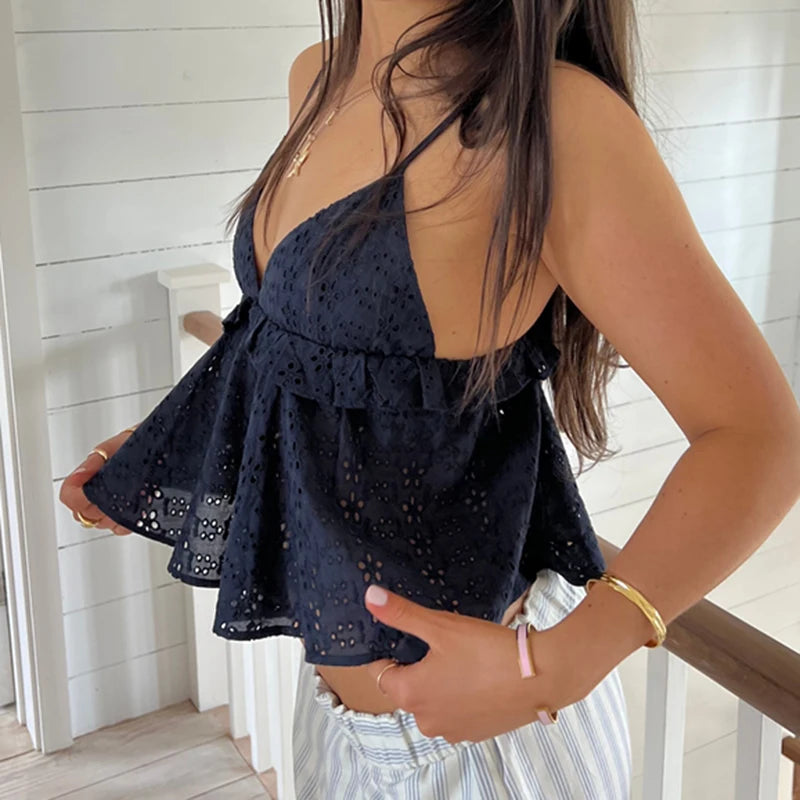 Woman wearing a navy blue sleeveless top with intricate detailing, standing indoors.