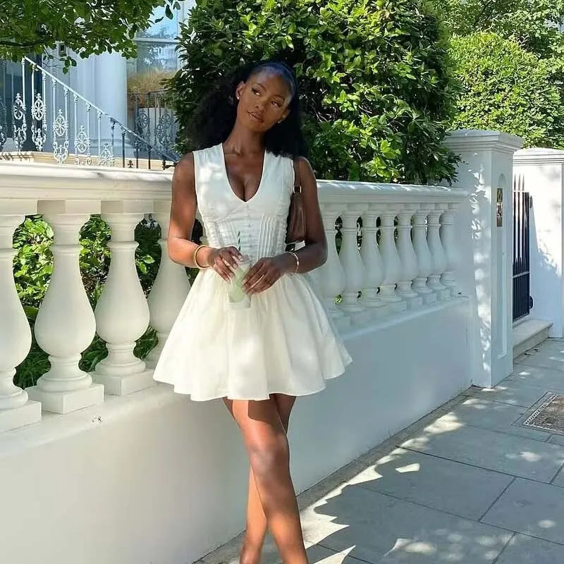 Woman in a white dress standing outdoors with greenery and a white railing in the background
