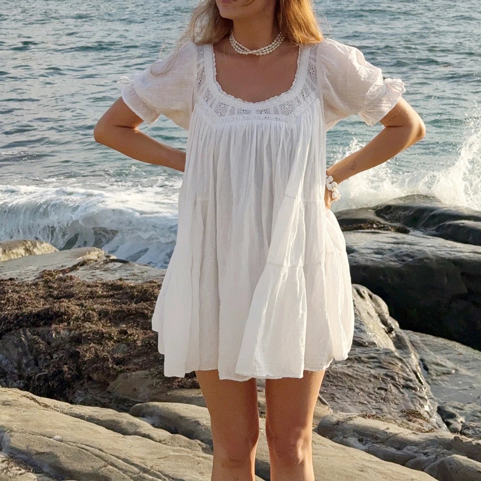 Woman in a white dress standing on rocks by the ocean
