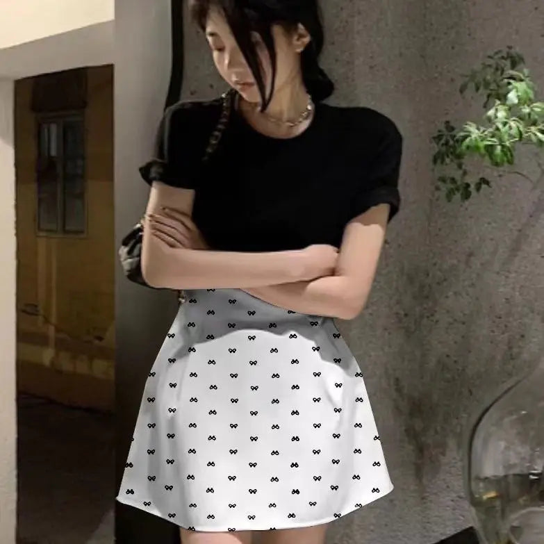 Person wearing a black top and white skirt with black patterns, standing against a textured wall.