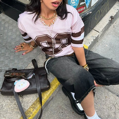 Person sitting on a curb wearing a white and brown sports jersey with large numbers, holding a black handbag.