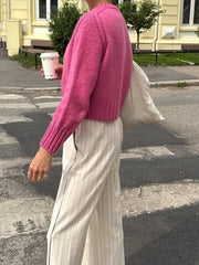 Person wearing a pink sweater and light-colored pants on a street.