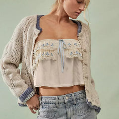 Woman wearing a beige embroidered top and cardigan with light blue jeans against a light green background