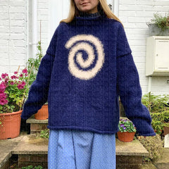 Person wearing a blue sweater with a white spiral design outdoors.