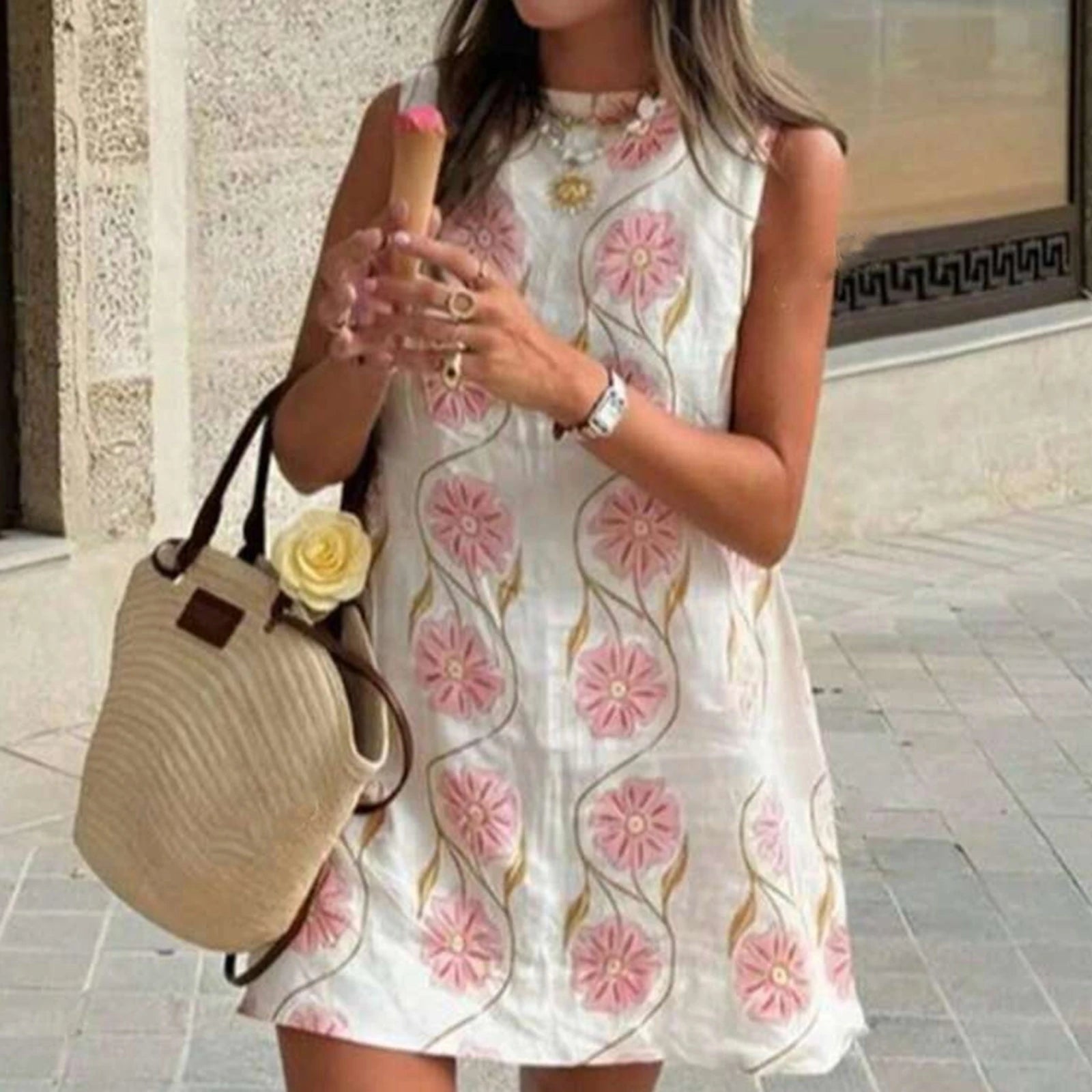 Woman in a floral dress holding a straw bag and phone, standing on a street.