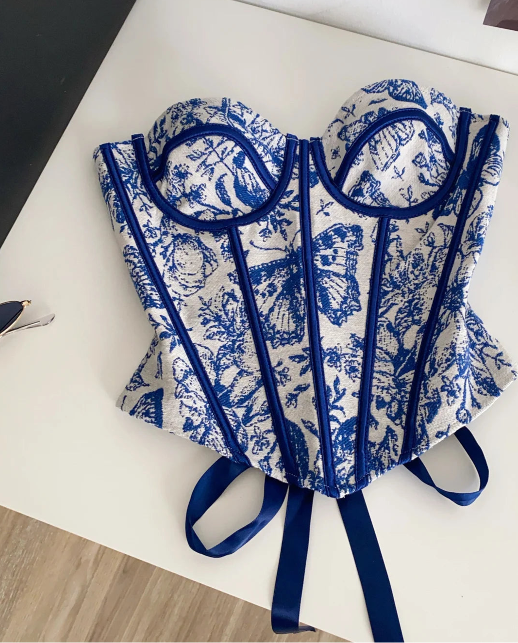 Blue and white patterned corset on a white surface with a black box in the background.