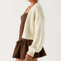 Person wearing a white knitted cardigan over a brown dress on a light gray background