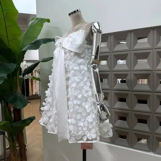 Side view of a white mini dress featuring a sheer overlay with delicate floral embellishments and a prominent satin bow on the bust.