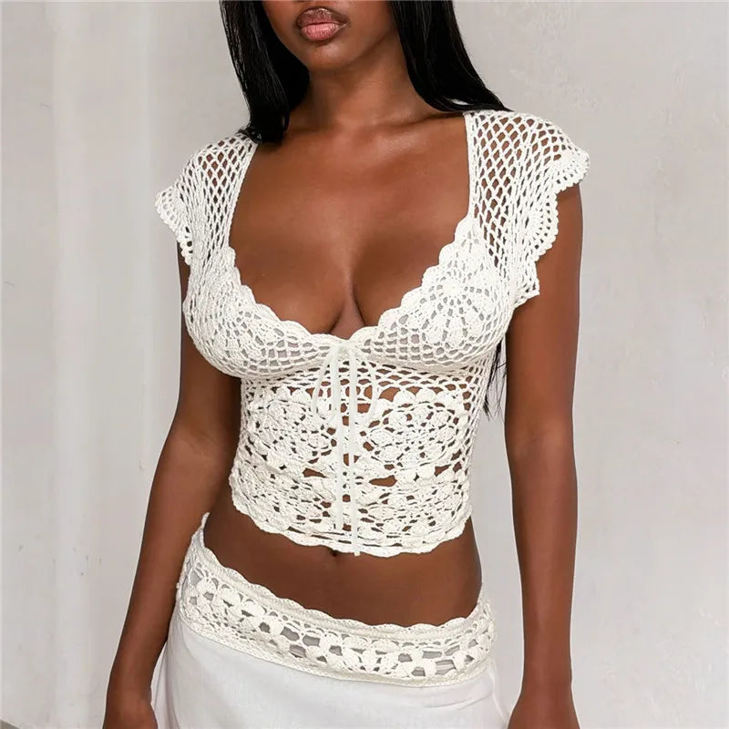 Close-up of a woman's torso wearing a white crochet crop top with intricate knit details and a low-cut neckline.