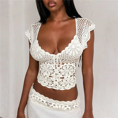 Close-up of a woman's torso wearing a white crochet crop top with intricate knit details and a low-cut neckline.