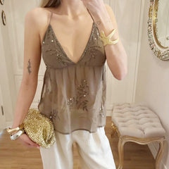Woman wearing a sheer top with embroidery and holding a gold clutch in a room.