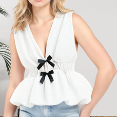 White sleeveless top with black bows worn by a person on a plain background