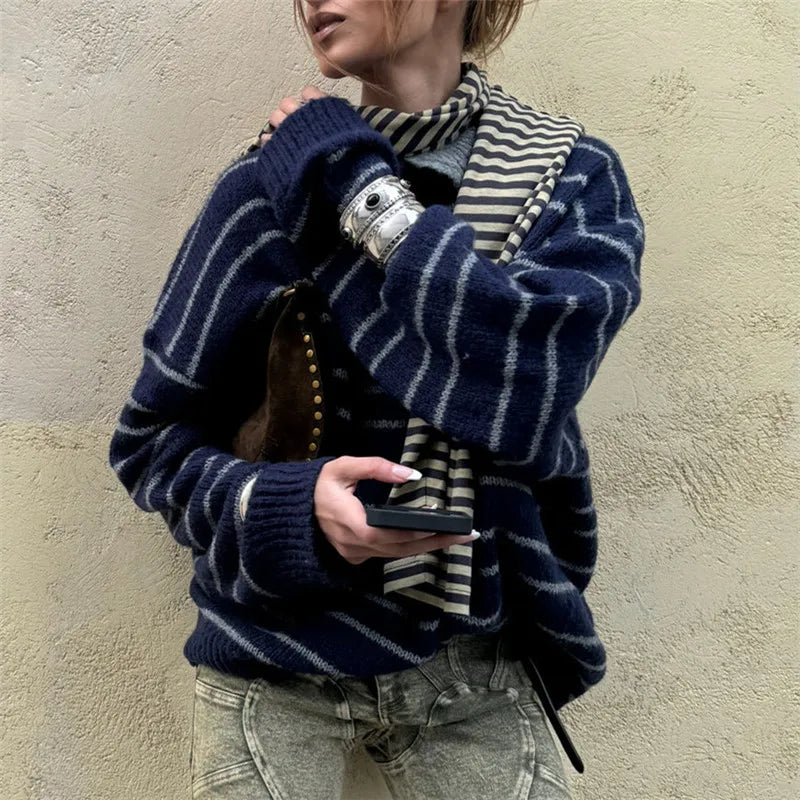 Person wearing a navy blue striped sweater and holding a phone against a beige wall.