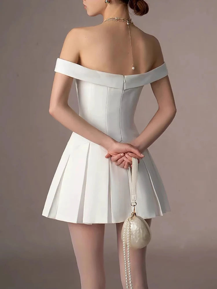 Woman wearing a white off-shoulder dress holding a matching handbag against a neutral background