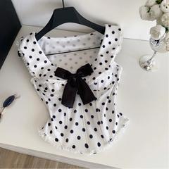 White blouse with black polka dots and a black bow on a white surface, with a  sunglasses in the background.