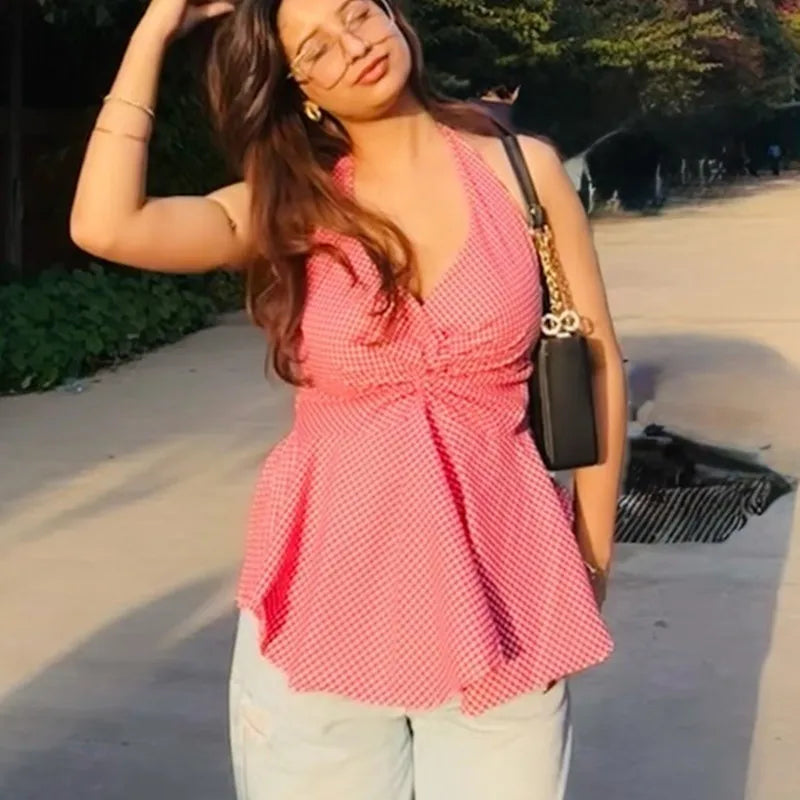 Woman wearing a pink gingham halter top with a twist front and peplum silhouette, paired with light wash jeans.