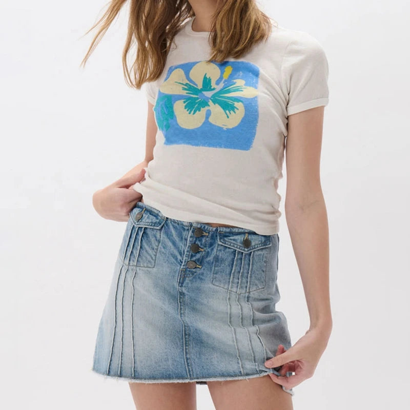 Person wearing a white t-shirt with a colorful graphic and a denim skirt 
