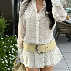 Woman wearing a white polka dot blouse and beige belt outdoors.