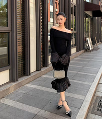 Woman in a black off-shoulder dress with ruffled details walking on a sidewalk.