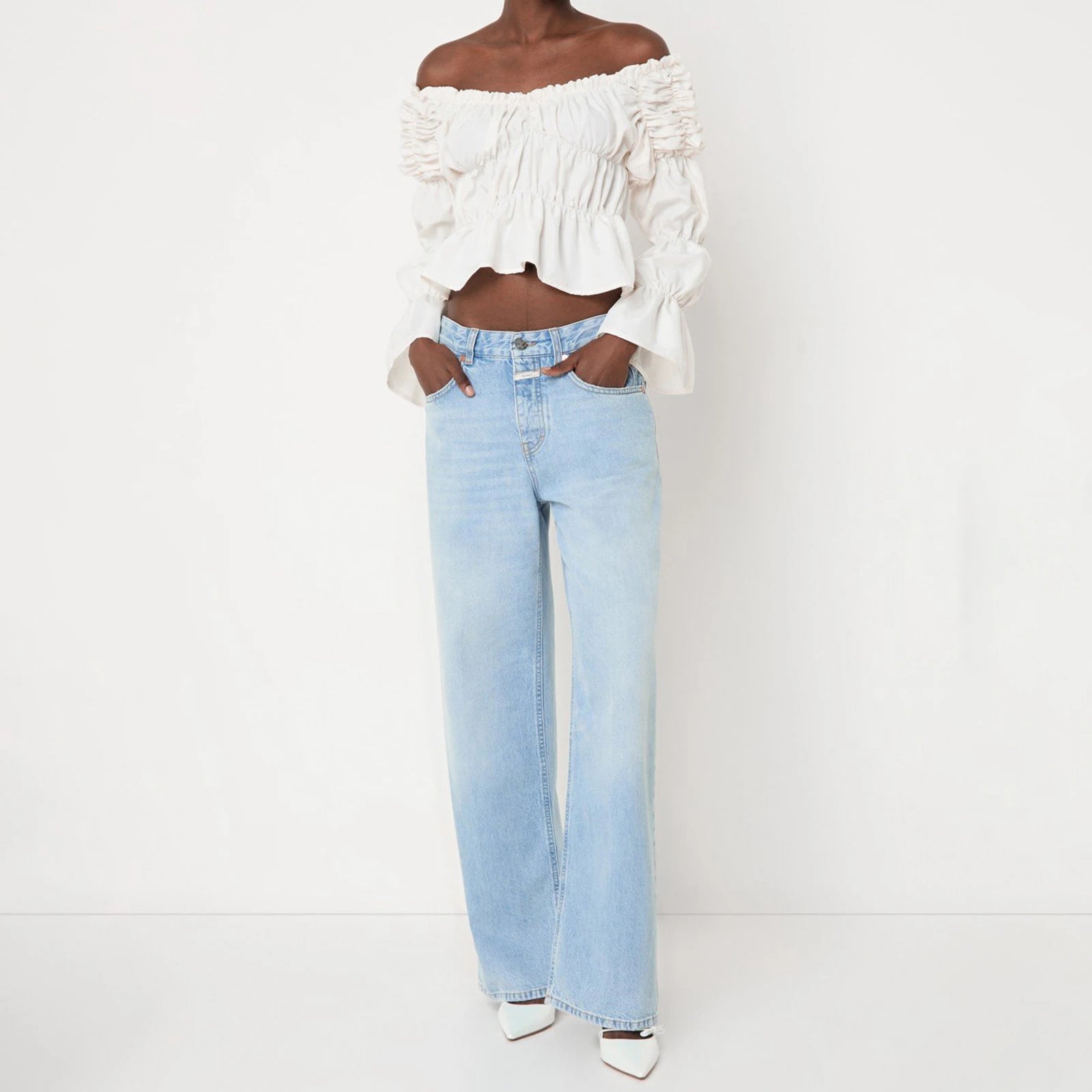 Person wearing a white off-shoulder top and light blue jeans 