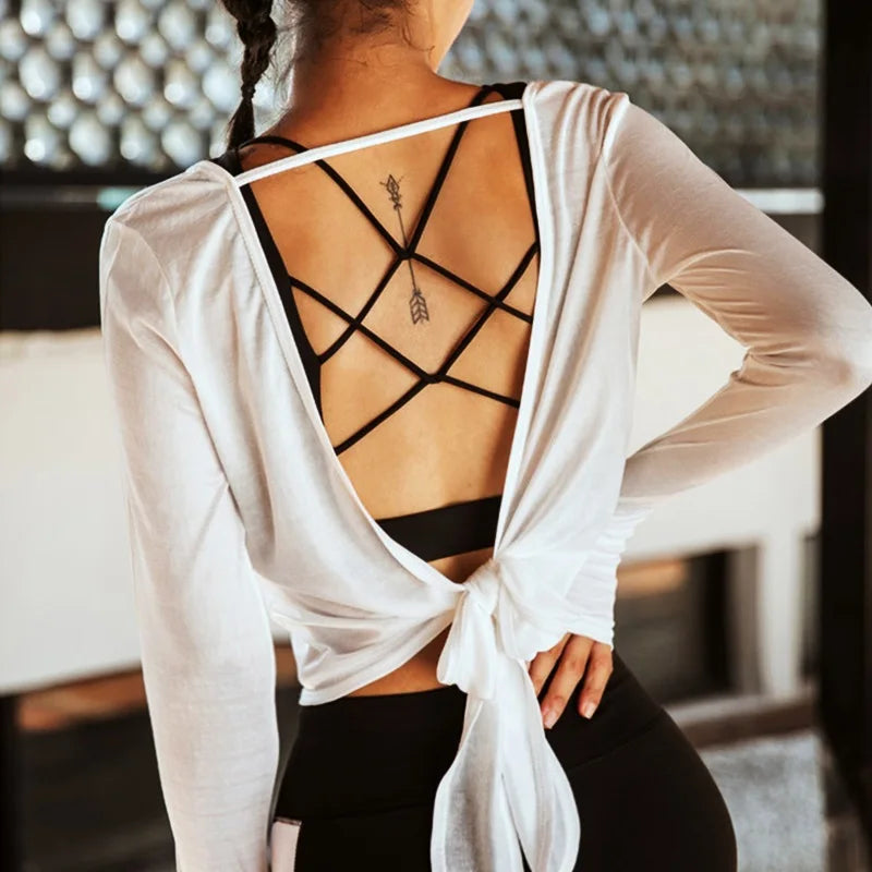 Person wearing a white long-sleeve top with a criss-cross back design over a black sports bra and leggings.