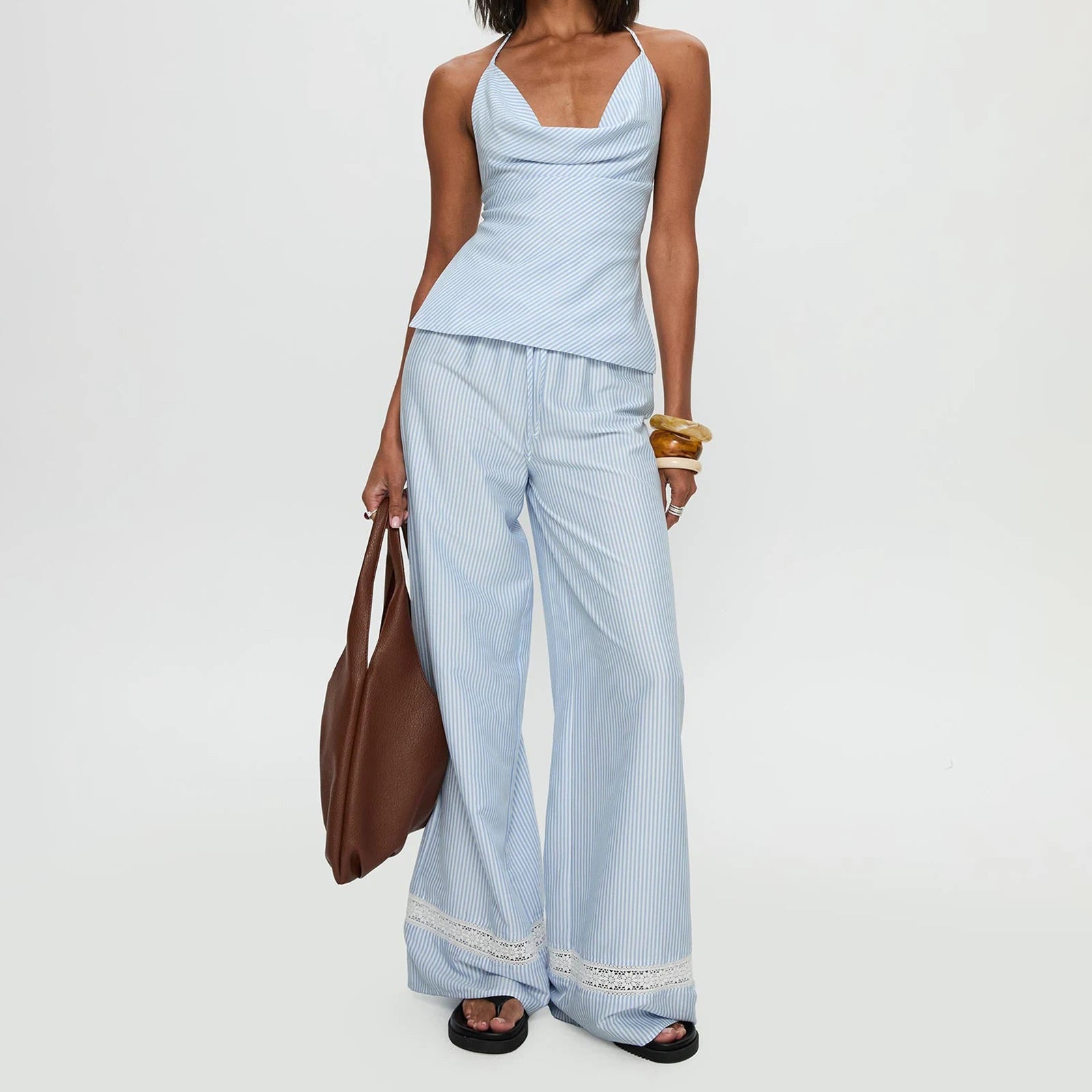 Woman wearing a light blue striped outfit with wide-leg pants and a brown bag 